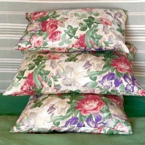 Trois coussins à motif roses et iris sur un canapé vert