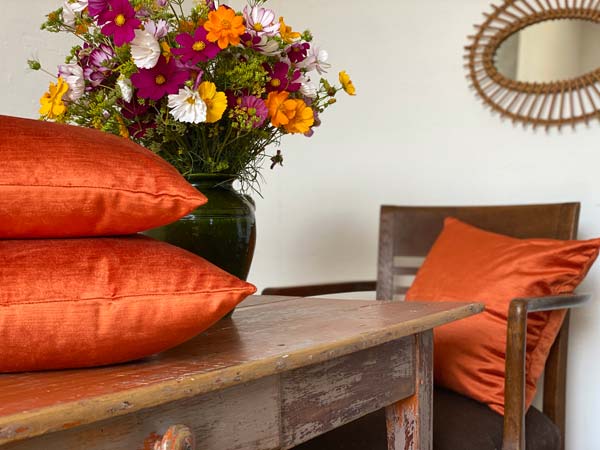 Coussins brillants couleur cuivre sur un table rustique avec un bouquet de fleurs aux couleurs de l'été indien